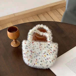 Sac à main blanc en peluche tricotée avec pompons colorés sur une table en bois