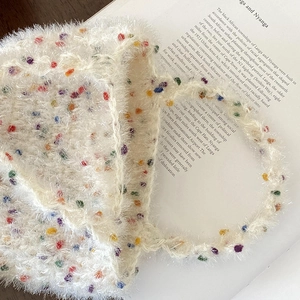 Gros plan d'un sac à main en peluche blanche à pois colorés sur un livre ancien