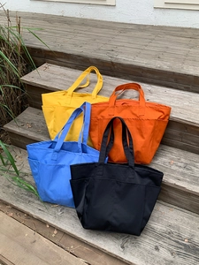 Grandi borse tote in nylon giallo, arancione, blu e nero su gradini in legno all'aperto
