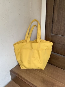 Dettaglio della borsa tote in nylon giallo con tasche frontali multiple e manici robusti