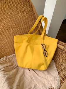 Dettaglio borsa tote in nylon giallo con tasche esterne e manici robusti per il trasporto