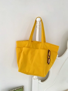 Dettaglio della borsa tote in nylon giallo con tasche appesa a un letto bianco
