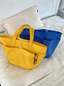 Dettaglio di grandi borse tote in nylon giallo e blu con tasche laterali su lenzuola chiare
