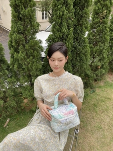 Quilted makeup bag detail with soft rhombus stitching and floral dress background