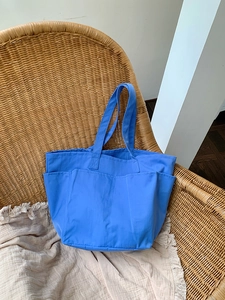 Dettaglio della borsa tote in nylon blu con tasche funzionali su sedia in rattan