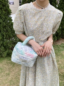 Close-up of quilted floral makeup bag with top handle shown in a sunny outdoor setting