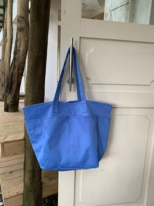 Dettaglio della borsa tote in nylon celeste con tasche multiple appesa a una porta bianca