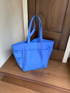 Dettaglio della borsa tote in nylon blu con tasche esterne su sfondo in legno naturale