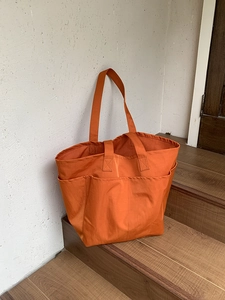 Dettaglio della borsa tote in nylon arancione con tasche esterne funzionali e manici