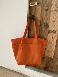 Dettaglio della borsa tote in tela arancione acceso con tre tasche frontali e cuciture rinforzate