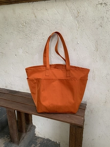 Grande borsa tote arancione in nylon con multitasche su panca di legno vintage