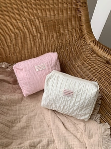 Detail of pink and white crinkle fabric cosmetic bags with tags on a woven chair