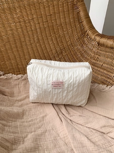Detail of white nylon pouch with pleated texture and pink patch on beige textile