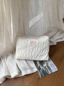 Detail of cream pleated nylon travel bag with text label on soft aesthetic background