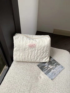 Detail of a beige pleated nylon makeup bag with a motivational quote label on a soft rug
