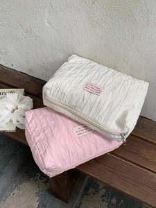 Quilted nylon cosmetic bags in pink and white with zipper and label on wooden bench