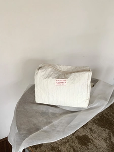 Detail view of a white quilted nylon cosmetic bag with elegant lettering on a label