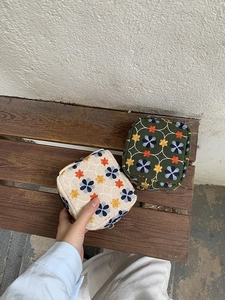 Detail of embroidered floral cosmetic pouches in beige and dark green on wood