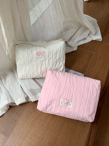 Detailed view of quilted nylon makeup bags in beige and pink on a warm wooden floor