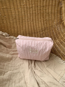 Close-up of pink pleated nylon makeup bag with decorative text patch and zipper detail