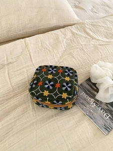 Detail of floral embroidery on olive green makeup bag with grid pattern and metal zipper