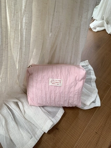 Pink pleated nylon storage bag with quote label on white draped curtain background