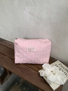 Detail of pink pleated nylon makeup bag with zipper and logo label on a wooden bench