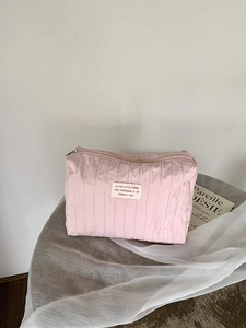 Detail of pink pleated nylon toiletry bag with zipper and woven label on a wooden table