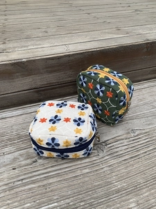 Detailed view of floral embroidery cosmetic bags with silver metal zippers on wood