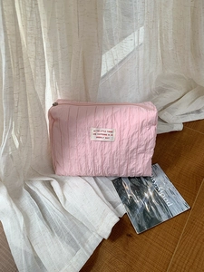 Detail of pink pleated nylon makeup bag with zipper closure and woven label on fabric