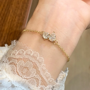 Elegant gold bracelet with dual pear-shaped zircons on a thin chain worn on wrist