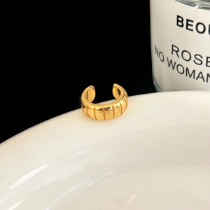 Close-up of golden C-shaped ear cuff with vertical striped texture on white porcelain