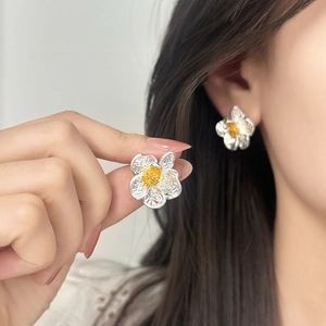 Elegant floral stud earrings with textured silver petals and yellow stamen on model