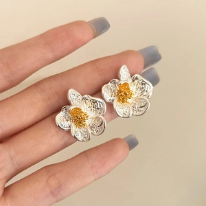 Detailed close-up of floral stud earrings with silver textured petals and golden stamen