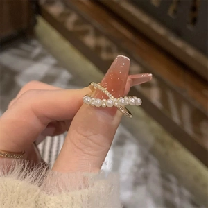 Gold crossover ring featuring elegant white pearls and pavé cubic zirconia on fingers