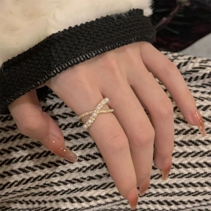 Detailed view of criss-cross golden ring with white pearls worn on a model's finger