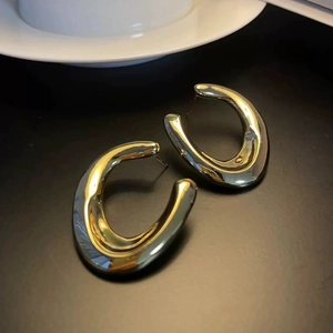 Macro detail of irregular gold C-shaped earrings with a high-polished metallic finish