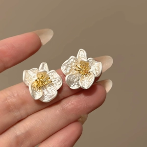 Elegant white flower stud earrings with textured petals and golden core held by hand