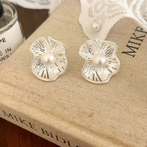 Close-up of floral silver earrings with white pearl center on vintage book cover