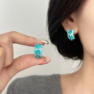 Chic silver earrings with light blue zircons shown on ear and held by hand