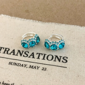 Detailed close-up of teal crystal huggie earrings with pave setting on fabric background