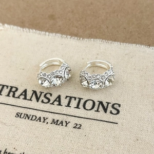 Detailed macro shot of silver zircon hoop earrings on a light fabric texture background