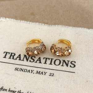 Close-up of golden hoop earrings with large champagne crystals and micro-pavé details