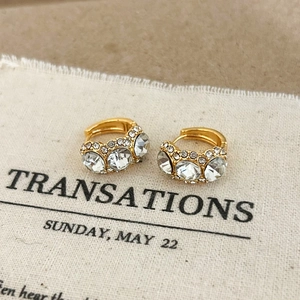 Close-up of gold-plated hoop earrings with large clear zircons on a textured background