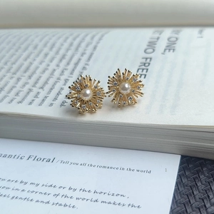 Vintage gold starburst earrings with central pearl and zircon accents on a book