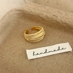 Detailed close-up of handmade gold multi-layer woven ring on rustic fiber background