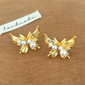 Detailed view of golden butterfly earrings with pearls and zircons on a textured background