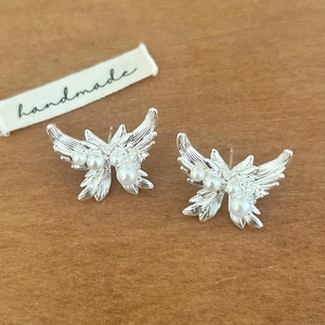 Detail of silver butterfly stud earrings featuring elegant white pearls on wood surface