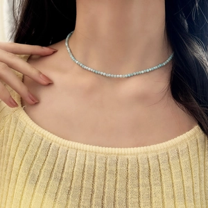 Close-up of light blue small beaded necklace worn by a model in yellow knitwear