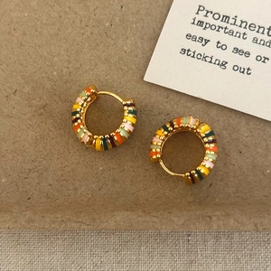 Détail de boucles d'oreilles créoles dorées avec émail coloré sur carte en papier